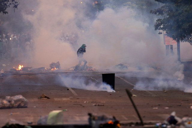 An anti-government protester runs through teargas during clashes in Caracas