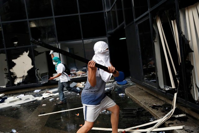 An anti-government protester breaks the windows of a public building in Caracas