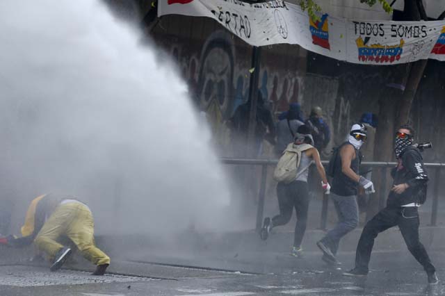 An anti-government protester is hit by water from a water cannon as another throws a molotov cocktail during riots in Caracas