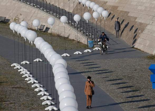 A woman walks under stands with balloons placed along the former Berlin Wall location by the Spree river, to be used in the installation 'Lichtgrenze' (Border of Light) in Berlin