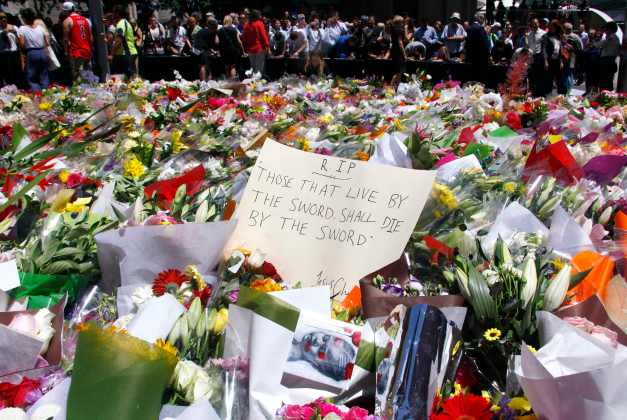 Members of the public stand behind a note that can be seen amongst floral tributes that have been placed near the cafe where hostages were held for over 16-hours, in Sydney