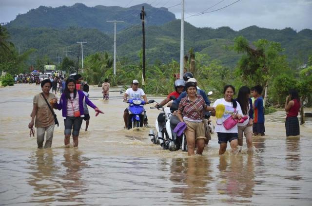 Varios vecinos de la localidad de Ormoc (Filipinas) caminan por las calles inundadas hoy, martes 30 de diciembre de 2014. Al menos ocho personas han muerto y más de 30.000 han tenido que abandonar sus hogares tras las inundaciones provocadas por la tormenta "Jangmi". EFE/Robert Dejon