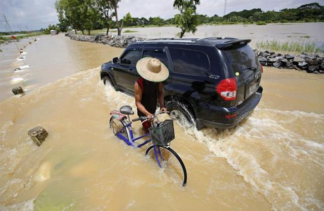 Un hombre tira de su bici junto a un coche que circula por las calles inundadas de Dar Ka (Birmania) hoy 12 de agosto de 2015. Casi un millón de personas se han visto damnificadas por las inundaciones que afectan gran parte de Birmania (Myanmar), provocadas por las intensas lluvias monzónicas que caen desde el mes pasado. El ministerio de Bienestar Social también indicó que el balance de víctimas ya superó el centenar, la mayoría de ellas en el estado Rakhine, en el oeste del país, según el diario Global New Light of Myanmar. EFE/Lynn Bo Bo