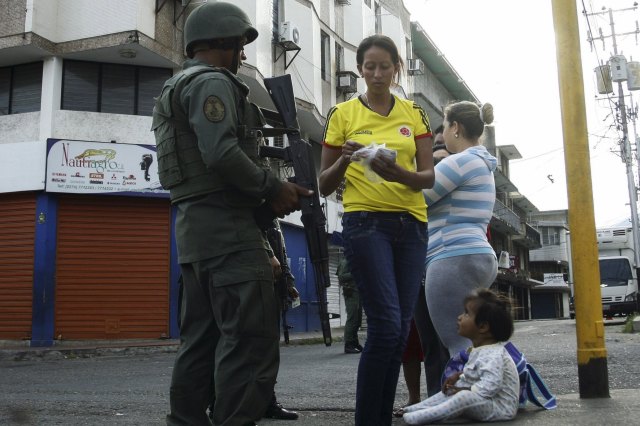 A woman looks for her identity card, next to a Venezuelan soldier at a checkpoint close to the border with Colombia, as part of a special deployment, at San Antonio in Tachira state, Venezuela August 22, 2015. Venezuela's closure of two border crossings with Colombia hurts innocent people, Colombia's President Juan Manuel Santos said on Saturday, adding that he hoped to speak to his Venezuelan counterpart Nicolas Maduro to find a solution. Maduro closed the crossings on Wednesday after a shootout between smugglers and troops left three soldiers wounded. He declared a 60-day state of emergency in five border municipalities on Friday. REUTERS/Carlos Eduardo Ramirez
