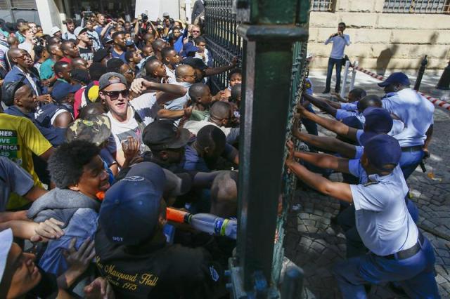 Estudiantes sudafricanos se enfrentan a la policía ante el Parlamento en Ciudad del Cabo (Sudáfrica) hoy, 21 de octubre de 2015. Miles de estudiantes sudafricanos que protestaban contra la subida del precio de las matrículas universitarias se enfrentaron hoy a la Policía frente a la sede del Parlamento, donde la sesión tuvo que ser suspendida. La Policía lanzó gas lacrimógeno y balas de goma para repeler a la multitud, que avanzaba hacia el edificio y había llegado hasta las escaleras de la Cámara, donde el ministro de Finanzas, Nhlanhla Nene, se dirigía a los diputados. EFE/Nic Bothma