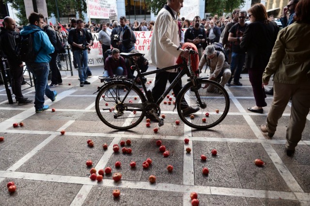 Un hombre empuja su bicicleta mientras camina por el Ministerio del Trabajo en el centro de Atenas el 05 de noviembre 2015 después que los estudiantes lanzaron tomates durante una protesta para llamar pidiendo más maestros y los fondos para la educación y en contra de las medidas de austeridad adicionales. Los plackards leen "sin ningún hambrientos alumnos-toman medidas ahora '. AFP PHOTO / LOUISA GOULIAMAKI