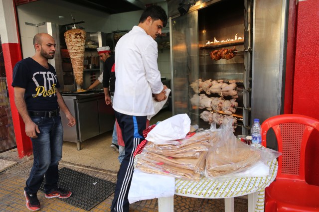 In this picture taken on Thursday, Nov. 26, 2015, Abdul Halim al-Attar, left, watches one of his employees, at his restaurant in Beirut, Lebanon. Abdul Halim al-Attar, a refugee from Syria who was photographed selling pens in the streets of Beirut, is now running three businesses in the city after an online crowdfunding campaign in his name collected $191,000. The 33-year-old father of two opened a bakery two months ago and has since added a kebab shop and a small restaurant to his business venture. (AP Photo/Hussein Malla)