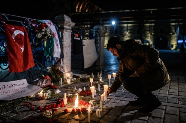 A man understood as Syrian living Istanbul lights a candle at a makeshift memorial with flowers and a Turkish and a Syrian flag in tribute to the victims of yesterday deadly attack, on January 13, 2016 on the site of the attack in the Istanbul's tourist hub of Sultanahmet.  Turkey said on January 13 it had arrested a total of five suspects over a deadly suicide bombing carried out by an Islamic State (IS) jihadist that killed 10 German tourists in the historic centre of Istanbul.  / AFP / OZAN KOSE