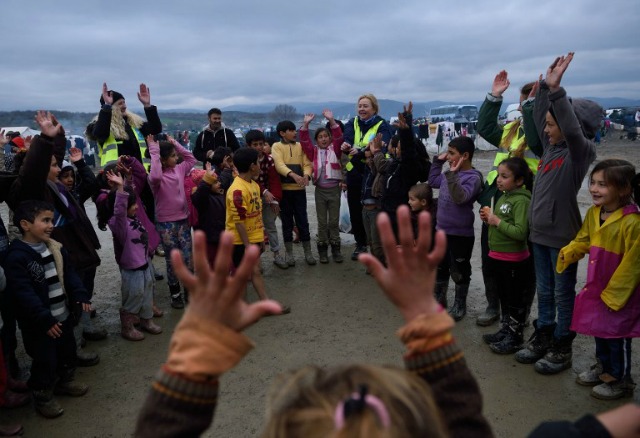 Los niños juegan con los trabajadores de las ONG en un campamento improvisado en la frontera entre Grecia y Macedonia, cerca de la localidad griega de Idomeni, el 16 de marzo de 2016, donde miles de refugiados y migrantes están varados por el bloqueo de la frontera de los Balcanes. Unos 1.500 migrantes que lograron cruzar a Macedonia, a pesar de la frontera está cerrada para ellos durante una semana, han sido enviados de vuelta a Grecia por las tropas macedonias, dijeron las autoridades el 15 de marzo. DANIEL MIHAILESCU / AFP