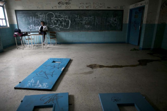 Fotografía del 1 de junio de 2016 muestra un estudiante sentado sobre el escritorio de un maestro dentro del que fue alguna vez un salón de clases, en el que hay puertas sobre el suelo, así como orina, en una escuela secundaria pública en Caracas, Venezuela. El caos social y económico que golpea Venezuela está desgarrando su alguna vez envidiable sistema escolar, robando a estudiantes pobres la que sería en caso contrario su mejor oportunidad de escapar de una vida cada vez más insoportable. (AP Foto/Ariana Cubillos)