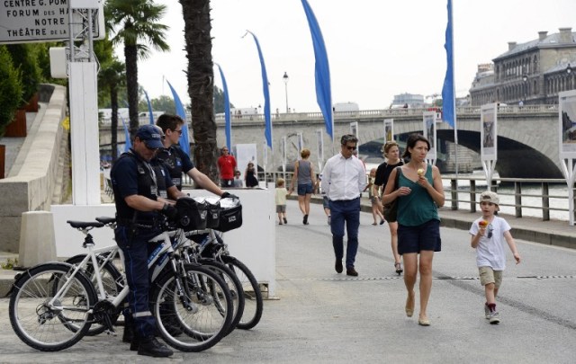 Policemen stand on their bikes as people walk in "Paris Plage" (Paris Beach) during the opening day of the event on the bank of the Seine river, in central Paris, on July 20, 2016. The 15th edition of Paris Plage will run until September 4, 2016. / AFP PHOTO / BERTRAND GUAY