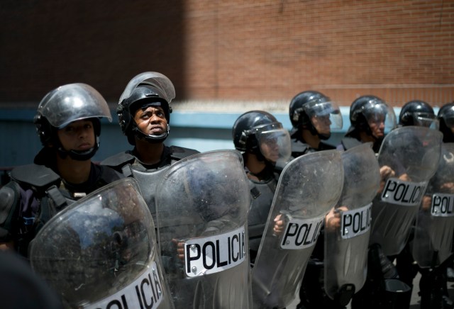 En esta fotografía del miércoles 7 de septiembre de 2016, un policía mira hacia manifestados apostados en lo alto de un edificio, mientras impide que otros manifestantes lleguen a la sede del Consejo Nacional Electoral, en Caracas, Venezuela. Los venezolanos han marchado en diversas ciudades del país para exigir que las autoridades permitan que se realice este año un referendo revocatorio contra el presidente Nicolás Maduro. (AP Foto/Ariana Cubillos)