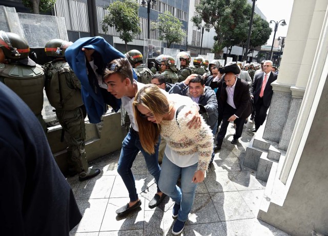 Opposition lawmakers protect themselves while they try to reach the National Assembly in Caracas on October 27, 2016. "We are going to notify Nicolas Maduro that the Venezuelan people declare he has abandoned his post," the speaker of the National Assembly, Henry Ramos Allup, said to cheers from hordes of protesters in Caracas. / AFP PHOTO / JUAN BARRETO