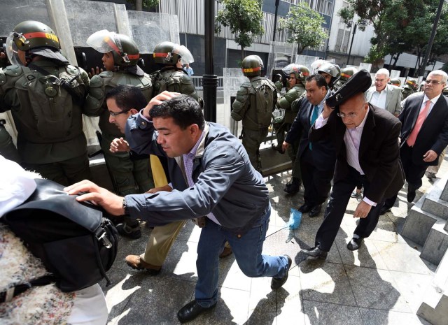 Opposition lawmakers protect themselves while they try to reach the National Assembly in Caracas on October 27, 2016. "We are going to notify Nicolas Maduro that the Venezuelan people declare he has abandoned his post," the speaker of the National Assembly, Henry Ramos Allup, said to cheers from hordes of protesters in Caracas. / AFP PHOTO / JUAN BARRETO