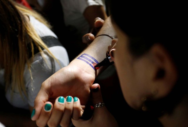 A woman paints the Cuban flag on someone's forearm during a massive tribute to Cuba's late President Fidel Castro on Revolution Square in Havana, Cuba, November 29, 2016. REUTERS/Stringer EDITORIAL USE ONLY. NO RESALES. NO ARCHIVE