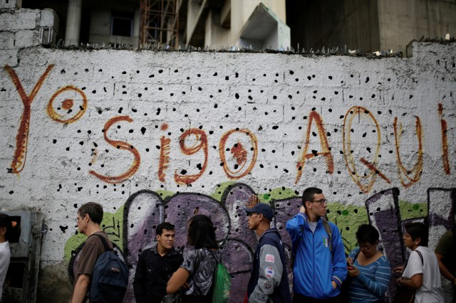 People line up to get into a Banco Mercantil branch next to a wall with a graffiti that reads "I'm still here" in Caracas, Venezuela December 13, 2016. REUTERS/Marco Bello