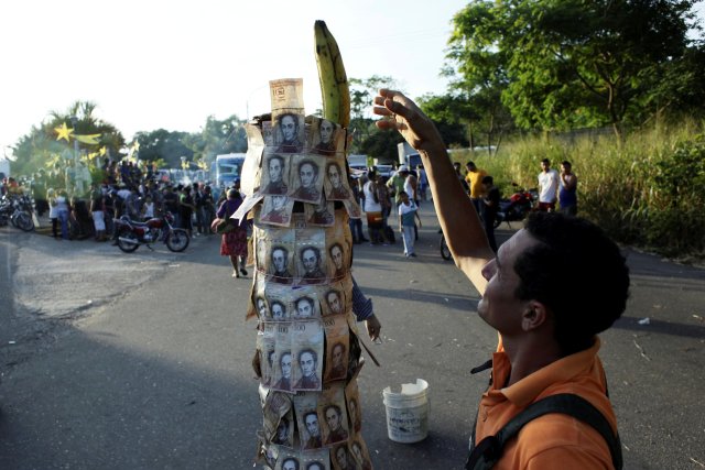 A man places a banana on a pole covered with 100-bolivar bills during a protest in El Pinal