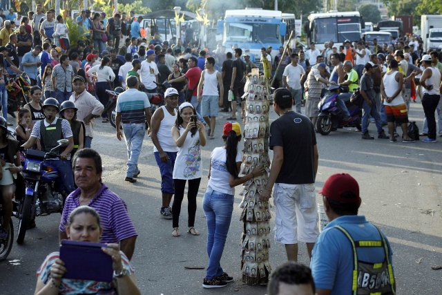 People take pictures next to a pole covered with 100-bolivar bills during a protest in El Pinal