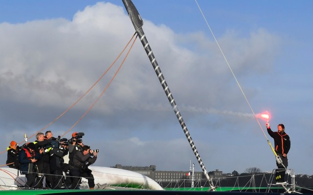 French skipper Thomas Coville (R) holds a flare as photographers take pictures onboard his "Sodebo Ultim'" multihull as he arrives in the port of Brest, western France, on December 26, 2016, after beating the record in solo non-stop round the world sailing. Coville, 48, slashed eight days off the record when he ended an astonishing solo non-stop circumnavigation of the World on his 31m maxi trimaran on December 25, 2016, in just 49 days, 3 hours, 7mins and 38secs.  / AFP PHOTO / Damien MEYER