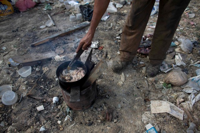 En esta imagen del 1 de noviembre de 2016, un hombre cocina piel de pollo que encontró en un basurero de Puerto Cabello, Venezuela la ciudad portuaria a la que llega la mayoría de la comida importada del país. Cuando la comida importada se estropea en puerto, el ejército intenta librarse de ella con discreción enterrándola en vertederos como este. Los vecinos dijeron que han podido recuperar avena, pipas de girasol y alimento para cerdos tirado por el ejército este año. (AP Foto/Ariana Cubillos)