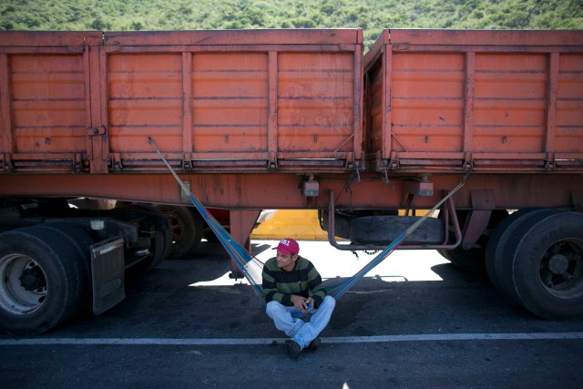 En esta imagen, tomada el 14 de noviembre de 2016, el conductor de un camión descansa en una hamaca bajo su vehículo mientras espera para entrar al puerto en Puerto Cabello, Venezuela, la ciudad a la que llega la mayoría de la comida que importa el país. A veces, los conductores tienen que esperar días para recoger la carga. Las demoras en la entrada al muelle son un castigo a los propietarios de las empresas de transporte que se niegan a pagar sobornos a los oficiales del ejército, según el presidente de la asociación de camioneros de Puerto Cabello, Jose Petit. (AP Foto/Ariana Cubillos)