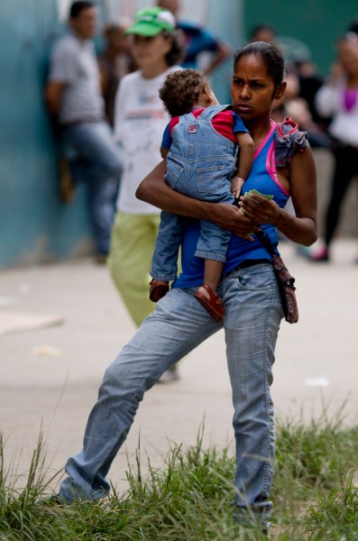 En esta imagen, tomada el 18 de noviembre de 2016, una mujer sostiene a su bebé en brazos mientras espera en el exterior de un supermercado para comprar comida subvencionada por el gobierno en Caracas, Venezuela. El ejército está utilizando su poder sobre el suministro de comida para enriquecerse, contribuyendo a una situación en la que los alimentos no llegan a la población que los necesita o, si está disponible, tiene precios desorbitados. (AP Foto/Ariana Cubillos)