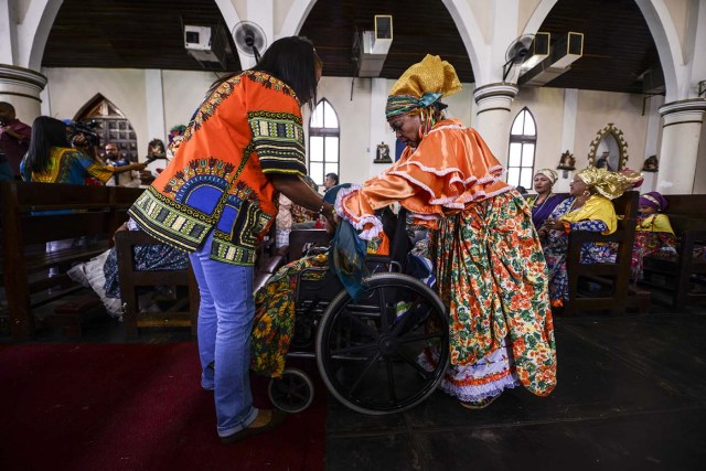 Women dressed as "madamas" attend a mass before the beginning of the Carnival in El Callao, in Bolivar state, Venezuela on February 26, 2017.  El Callao's carnival was recently named Unesco's Intangible Cultural Heritage of Humanity and is led by the madamas, the pillars of Callaoense identity representing Antillean matrons considered the communicators of values, who dance and wear colourful dresses. / AFP PHOTO / JUAN BARRETO