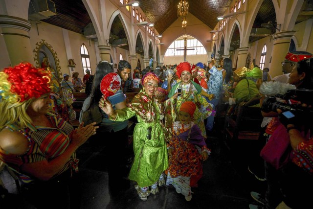 Women dressed as "madamas" attend a mass before the beginning of the Carnival in El Callao, Bolivar state, Venezuela on February 26, 2017.  El Callao's carnival was recently named Unesco's Intangible Cultural Heritage of Humanity and is led by the madamas, the pillars of Callaoense identity representing Antillean matrons considered the communicators of values, who dance and wear colourful dresses. / AFP PHOTO / JUAN BARRETO