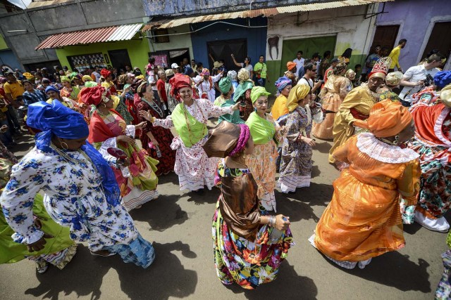 Women dressed as "madamas" dance as they take part in a parade during the Carnival in El Callao, Bolivar state, Venezuela on February 26, 2017.  El Callao's carnival was recently named Unesco's Intangible Cultural Heritage of Humanity and is led by the madamas, the pillars of Callaoense identity representing Antillean matrons considered the communicators of values, who dance and wear colourful dresses. / AFP PHOTO / JUAN BARRETO