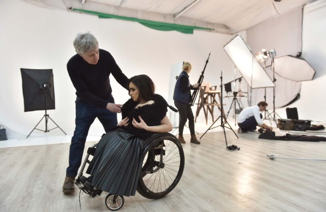 TO GO WITH AFP STORY BY OLGA SHYLENKO Ukrainian fashion designer Fedir Vozianovmakes (L) makes adjustments to a creation worn by Ukrainian model Alexandra Kutas, who is in a wheelchair from a very early age due to a spinal cord injury resulting from a doctor's mistake at birth, prior to a photo and video fashion shoot in Kiev on January 25, 2017. Kutas, 23, is Ukraine's first model with a disability to headline a runway event of this level, after covering a long and thorny path for her dream to come true. / AFP PHOTO / Sergei SUPINSKY / ?The erroneous mention[s] appearing in the metadata of this photo by Sergei SUPINSKY has been modified in AFP systems in the following manner: [a spinal cord injury resulting from a doctor's mistake at birth] instead of [cerebral palsy]. Please immediately remove the erroneous mention[s] from all your online services and delete it (them) from your servers. If you have been authorized by AFP to distribute it (them) to third parties, please ensure that the same actions are carried out by them. Failure to promptly comply with these instructions will entail liability on your part for any continued or post notification usage. Therefore we thank you very much for all your attention and prompt action. We are sorry for the inconvenience this notification may cause and remain at your disposal for any further information you may require.?