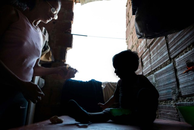 The mother of Venezuelan Rebeca Leon, who scavanges for food in the streets of Caracas, feeds her grandson at their house in Petare shantytown, on February 22, 2017. Venezuelan President Nicolas Maduro is resisting opposition efforts to hold a vote on removing him from office. The opposition blames him for an economic crisis that has caused food shortages. / AFP PHOTO / FEDERICO PARRA / TO GO WITH AFP STORY by Alexander Martinez