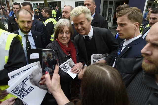 Dutch far-right Freedom Party leader (Partij Voor De Vrijheid, PVV) Geert Wilders is guarded by police as he poses with a supporter in Heerlen on March 11, 2017. Wilders was guarded by police as protesters took to the streets while he handed out pamphlets and posed for selfies as part of his election campaign. / AFP PHOTO / JOHN THYS