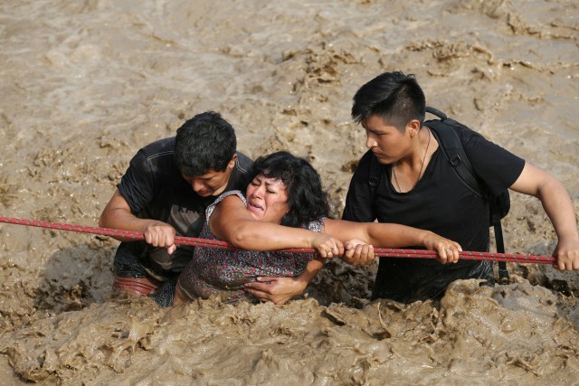 REFILE - CORRECTING NAME OF THE RIVER A woman is assisted while crossing a flooded street after the Huaycoloro river overflooded its banks sending torrents of mud and water rushing through the streets in Huachipa, Peru, March 17, 2017. REUTERS/Guadalupe Pardo TPX IMAGES OF THE DAY