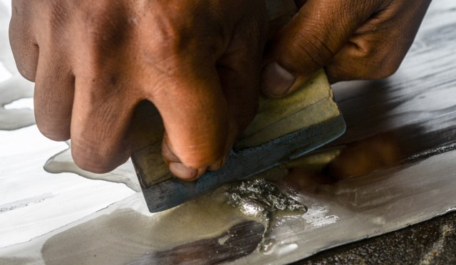 A worker scrapes gold-mercury amalgam from an aluminium sheet at a gold mine in El Callao, Bolivar state, southeastern Venezuela on February 25, 2017. Although life in the mines of eastern Venezuela is hard and dangerous, tens of thousands from all over the country head for the mines daily in overcrowded trucks, pushed by the rise in gold prices and by the severe economic crisis affecting the country, aggravated recently by the drop in oil prices. / AFP PHOTO / JUAN BARRETO / TO GO WITH AFP STORY by Maria Isabel SANCHEZ