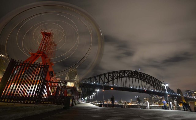 The ferris wheel at Luna Park and Sydney Harbour Bridge are plunged into darkness for the Earth Hour environmental campaign in Sydney on March 25, 2017. The lights went out on two of Sydney's most famous landmarks for the 10th anniversary of the climate change awareness campaign Earth Hour, among the first landmarks around the world to dim their lights for the event. / AFP PHOTO / PETER PARKS