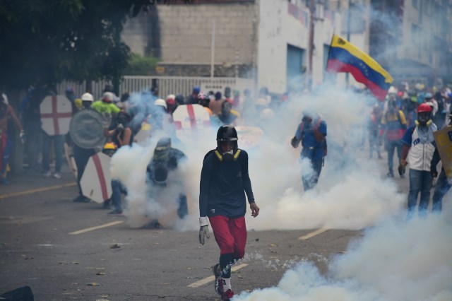 Engulfed in a cloud of tear gas shot by riot police, opposition demonstrators take cover behind makeshift shields during a protest against Venezuelan President Nicolas Maduro, in Caracas on May 3, 2017. Venezuela's angry opposition rallied Wednesday vowing huge street protests against President Nicolas Maduro's plan to rewrite the constitution and accusing him of dodging elections to cling to power despite deadly unrest. / AFP PHOTO / RONALDO SCHEMIDT