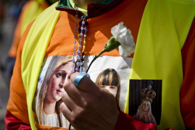 A pilgrim sporting a t-shirt with the image of Our Lady of Fatima, holds a carnation at Fatima, central Portugal, on May 11, 2017.  Two of the three child shepherds who reported apparitions of the Virgin Mary in Fatima, Portugal, one century ago, will be declared saints on May 13, 2017 by Pope Francis. The canonisation of Jacinta and Francisco Marto will take place during the Argentinian pontiff's visit to a Catholic shrine visited by millions of pilgrims every year. / AFP PHOTO / PATRICIA DE MELO MOREIRA