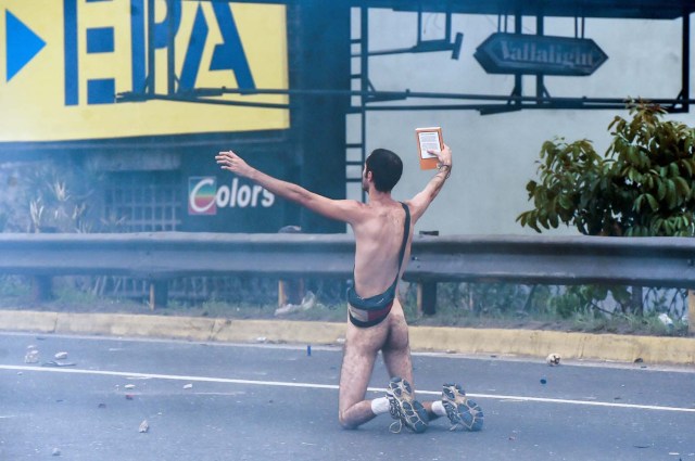 EDITORS NOTE: Graphic content / (FILES) This file photo taken on April 20, 2017 shows a naked demonstrator taking part in a protest against Venezuelan President Nicolas Maduro, in Caracas on April 20, 2017. Wearing nothing but white sports shoes and socks, a money belt and an anguished expression, Hans Wuerich, 27, raised a bible in his skinny hand as he stood on top of a police armored car on April 20. "I'm not some flower-power hippy," he told AFP later. "But I do believe that peaceful protest does more harm to the government than violence. I stunned them." / AFP PHOTO / JUAN BARRETO