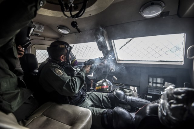 A Venezuelan National Guard soldier fires his shotgun at opposition demonstrators from inside their riot control vehicle, in Caracas, on May 31, 2017. Venezuelan authorities on Wednesday began signing up candidates for a planned constitutional reform body, a move that has inflamed deadly unrest stemming from anti-government protests. / AFP PHOTO / JUAN BARRETO