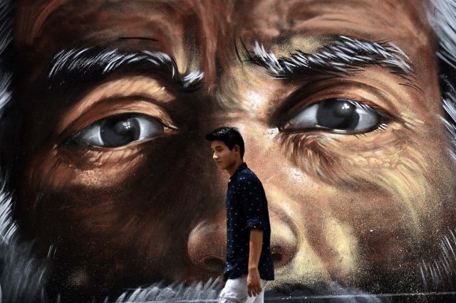 A young man passes by a gratfiti in Cancun, Mexico,  on June 18, 2017. / AFP PHOTO / PEDRO PARDO