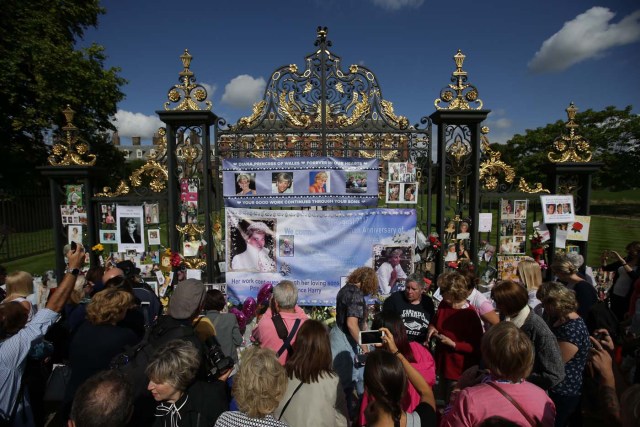 Members of the public gather at the tributes of flowers, candles and photographs outside one of the gates of Kensington Palace in London on August 31, 2017, to mark the 20th anniversary of the death of Diana, Princess of Wales. Tributes of photographs, candels and photographs have gathered at the gates of Kensington Palace left by well-wishers and fans of Diana, princess of Wales to mark the 20th anniversary of her death on August 31, 2017. The Princess of Wales died in a fatal car crash in Paris on August 31, 1997. Well-wishers and fans of Diana visited the palace in the early hours of the morning on August 31 to pay their respects with a vigil at the famous gates of Diana's former residence. / AFP PHOTO / Daniel LEAL-OLIVAS