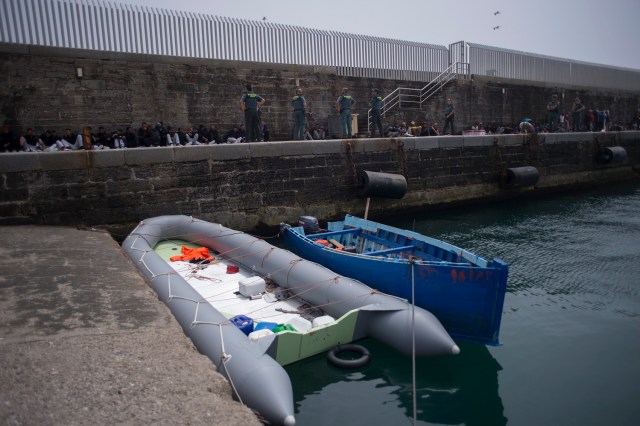 Two makeshift boats moor in foreground as would-be immigrants rest after being rescued in the waters of the Strait of Gibraltar, in the port of Tarifa, on August 16, 2017. Since 1am today, the Spanish rescue services gathered 339 persons who were trying to reach Spain on board seven makeshift boats. / AFP PHOTO / JORGE GUERRERO