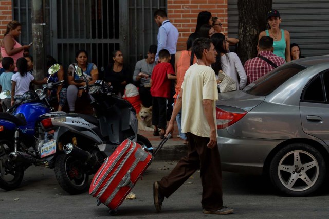 A man carries the suitcase of a passenger at a bus station in Caracas on October 11, 2017 as scores of disappointed Venezuelans who see no end to the crisis choose to leave the country. Venezuela, which holds regional elections on October 15, is a country at the top of the Latin American continent that is in deep economic and political crisis. / AFP PHOTO / Federico PARRA