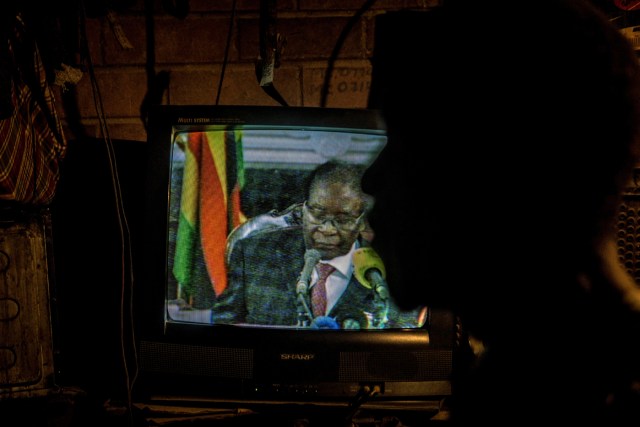 Un hombre mira un televisor que transmite un discurso estatal del presidente de Zimbabwe, Robert Mugabe, en Mbare, Harare, el 19 de noviembre de 2017. El presidente de Zimbabue, Robert Mugabe, en una muy esperada conferencia televisiva, destacó que aún estaba en el poder después de que su régimen autoritario de 37 años se vio sacudido por una toma militar. Muchos zimbabuenses esperaban que Mugabe renunciara luego de que el ejército tomara el poder la semana pasada. Pero Mugabe pronunció su discurso junto a los generales uniformados que estaban detrás de la intervención militar. En su discurso, Mugabe no hizo referencia al clamor por su renuncia. / AFP PHOTO / ZINYANGE AUNTONY