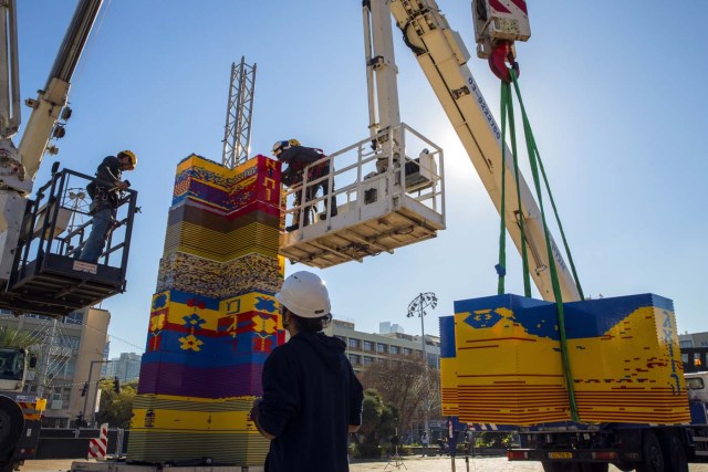 Workers and volunteers help assemble bricks during the construction of a LEGO tower in Tel Aviv's Rabin Square on December 26, 2017, as the city attempts to break Guinness world record of the highest such structure. / AFP PHOTO / JACK GUEZ