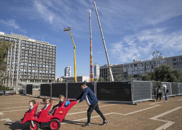 A man pushes a child stroller as he passes by a LEGO tower under construction in Tel Aviv's Rabin Square on December 27, 2017, as the city attempts to break Guinness world record of the highest such structure. / AFP PHOTO / JACK GUEZ