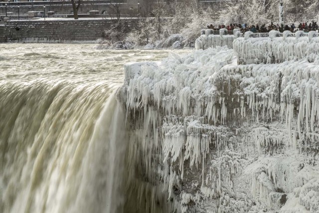 Tourists take photos of the Horseshoe Falls in Niagara Falls, Ontario on January 3, 2018. The cold snap which has gripped much of Canada and the United States has nearly frozen over the American side of the falls. / AFP PHOTO / Geoff Robins