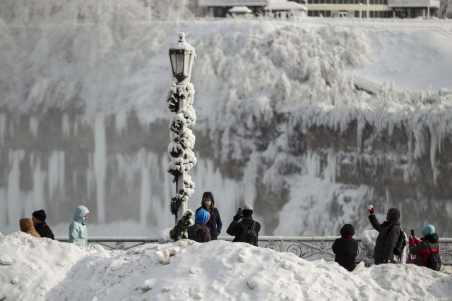 Tourists take photos of the Horseshoe Falls in Niagara Falls, Ontario on January 3, 2018. The cold snap which has gripped much of Canada and the United States has nearly frozen over the American side of the falls. / AFP PHOTO / Geoff Robins