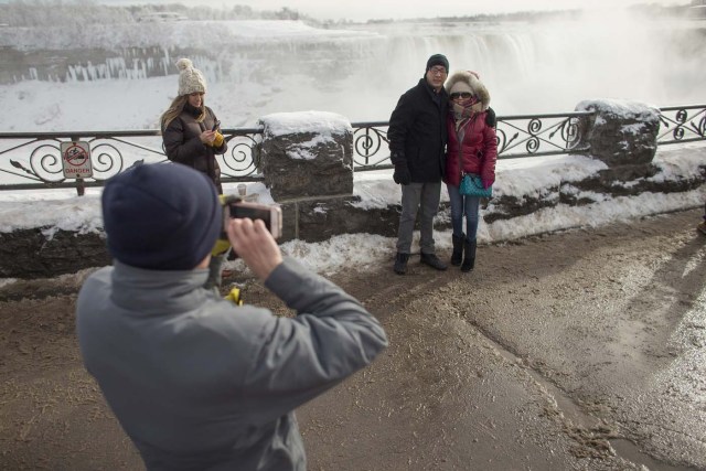 Tourists take photos of the Horseshoe Falls in Niagara Falls, Ontario on January 3, 2018. The cold snap which has gripped much of Canada and the United States has nearly frozen over the American side of the falls. / AFP PHOTO / Geoff Robins