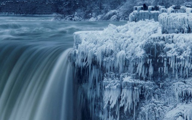 A lone visitor takes a picture near the brink of the ice covered Horseshoe Falls in Niagara Falls, Ontario, Canada, January 3, 2018. REUTERS/Aaron Lynett